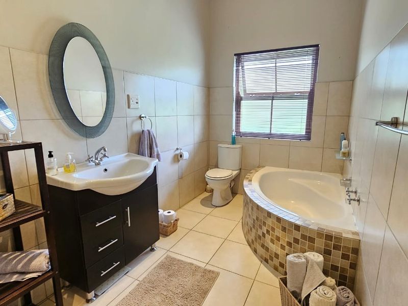 A functional bathroom featuring a vanity cabinet, built-in bathtub with mosaic tile detailing, toilet, and neutral ceramic wall and floor tiling.