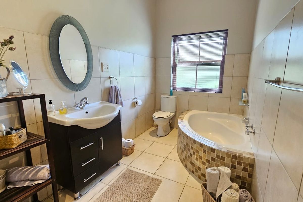 A functional bathroom featuring a vanity cabinet, built-in bathtub with mosaic tile detailing, toilet, and neutral ceramic wall and floor tiling.