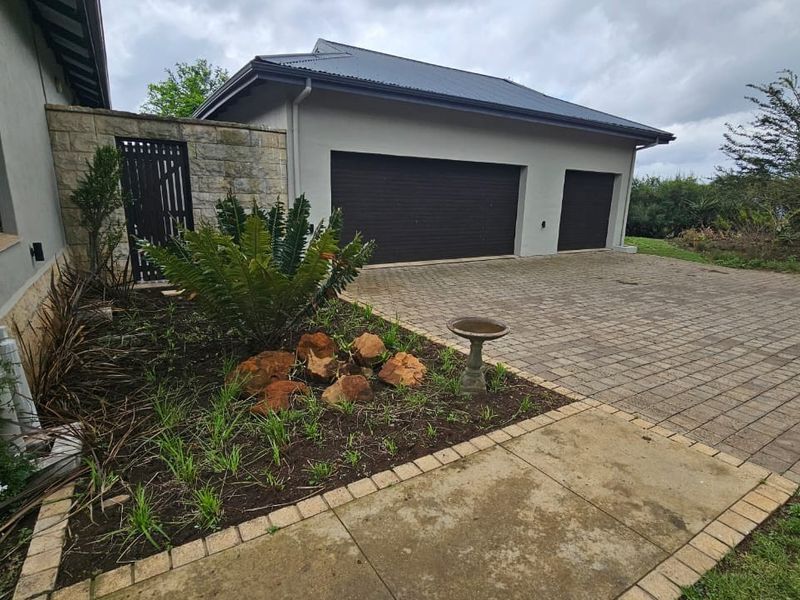 A well-maintained exterior view featuring a double garage, paved driveway, and stone-clad accents, complemented by landscaped garden beds.