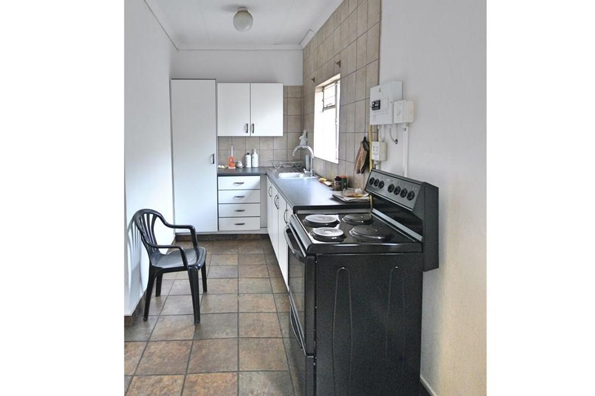 A functional galley-style kitchen featuring built-in cabinetry, tiled splashbacks, a stainless steel sink, and a freestanding electric stove.
