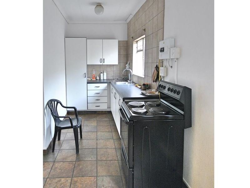 A functional galley-style kitchen featuring built-in cabinetry, tiled splashbacks, a stainless steel sink, and a freestanding electric stove.