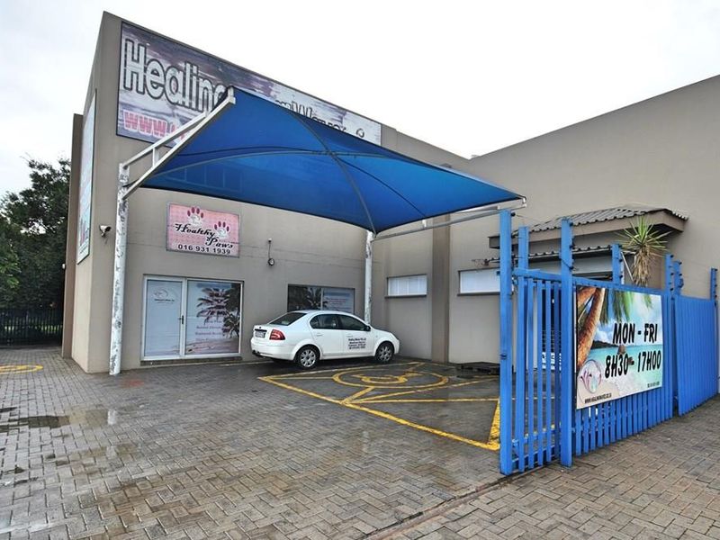 Commercial property exterior featuring a paved parking area, blue shade sail structure, and secure gated entrance with business signage.
