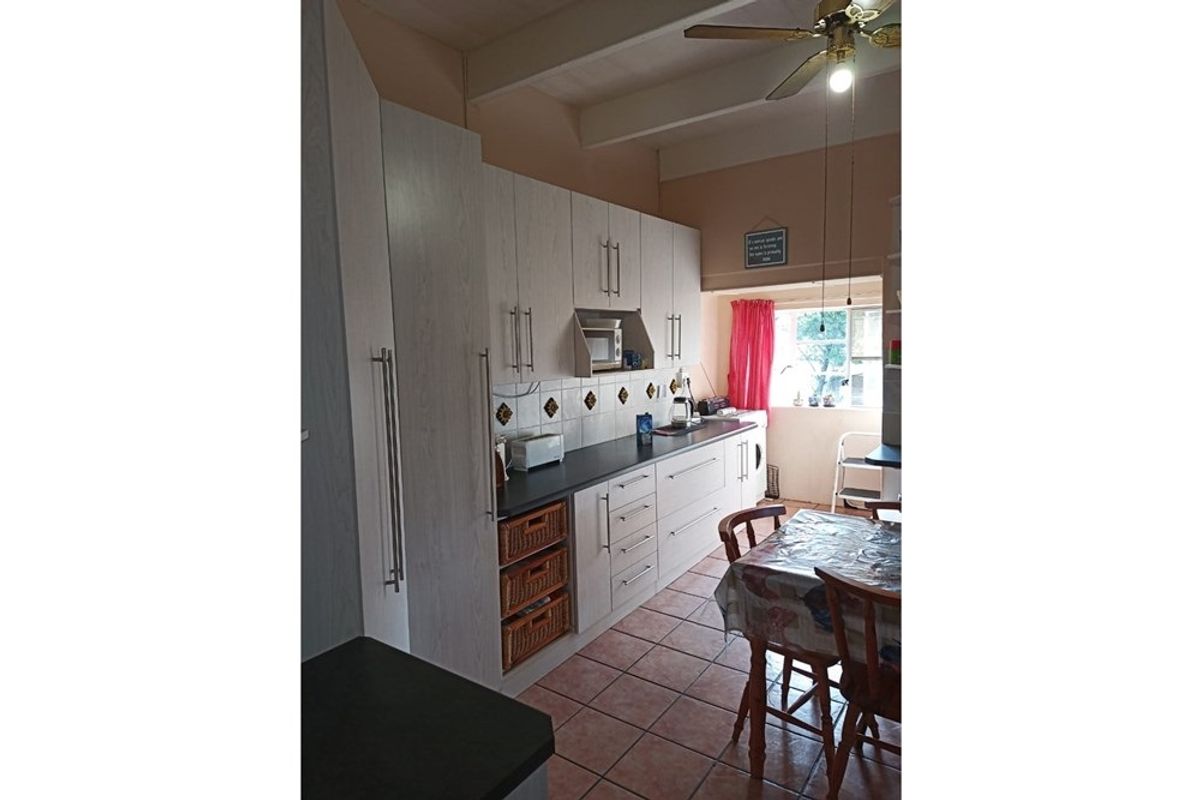 A functional kitchen featuring light-toned cabinetry, dark countertops, tiled flooring, and a ceiling fan, offering a practical layout for daily meal preparation.
