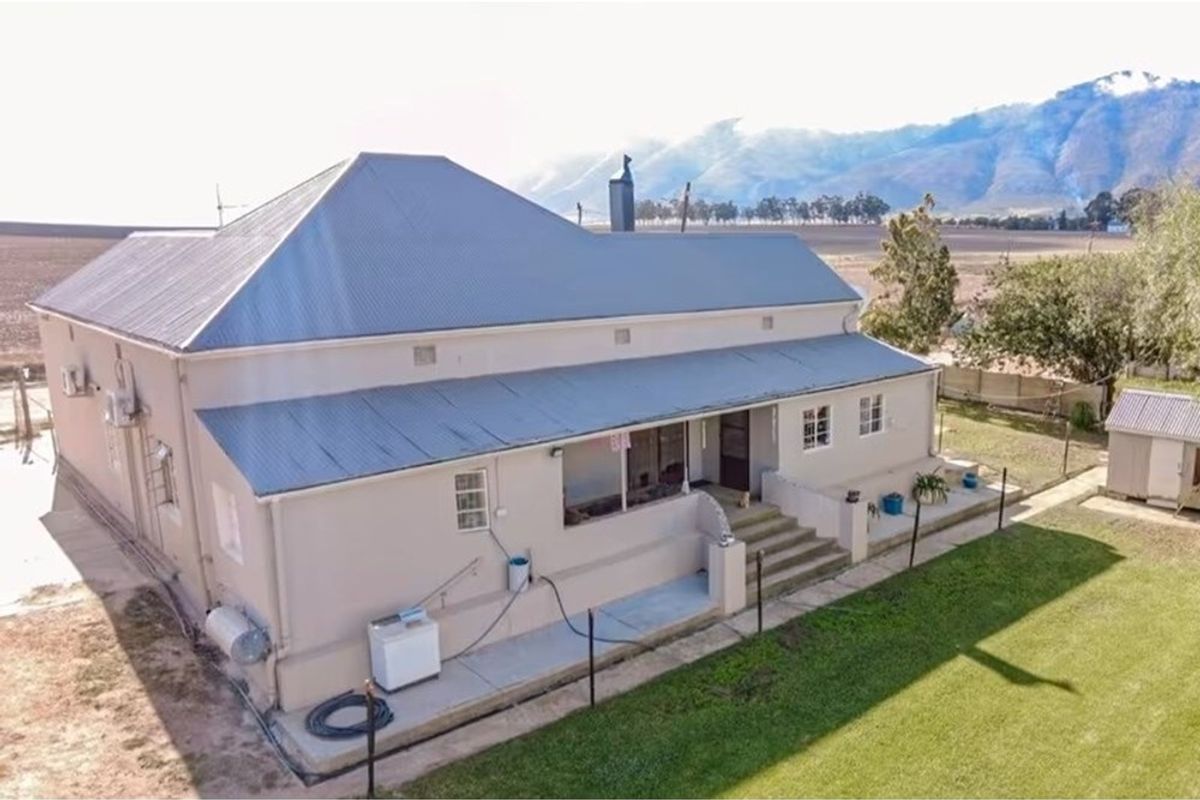 Aerial view of the rear elevation of a small holding property, featuring a corrugated metal roof, covered patio, and surrounding garden area.
