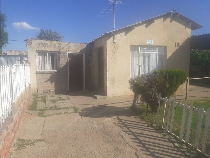Front view of a single-story residential property featuring a concrete driveway, picket fencing, and plastered exterior walls.