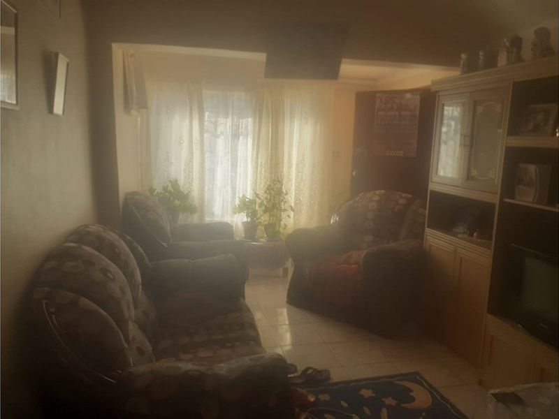 A dimly lit living room featuring tiled flooring and natural light filtering through window curtains.