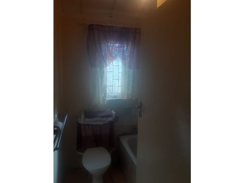 A compact bathroom featuring a bathtub and toilet, requiring updated lighting and finishes to improve the overall aesthetic and functionality.