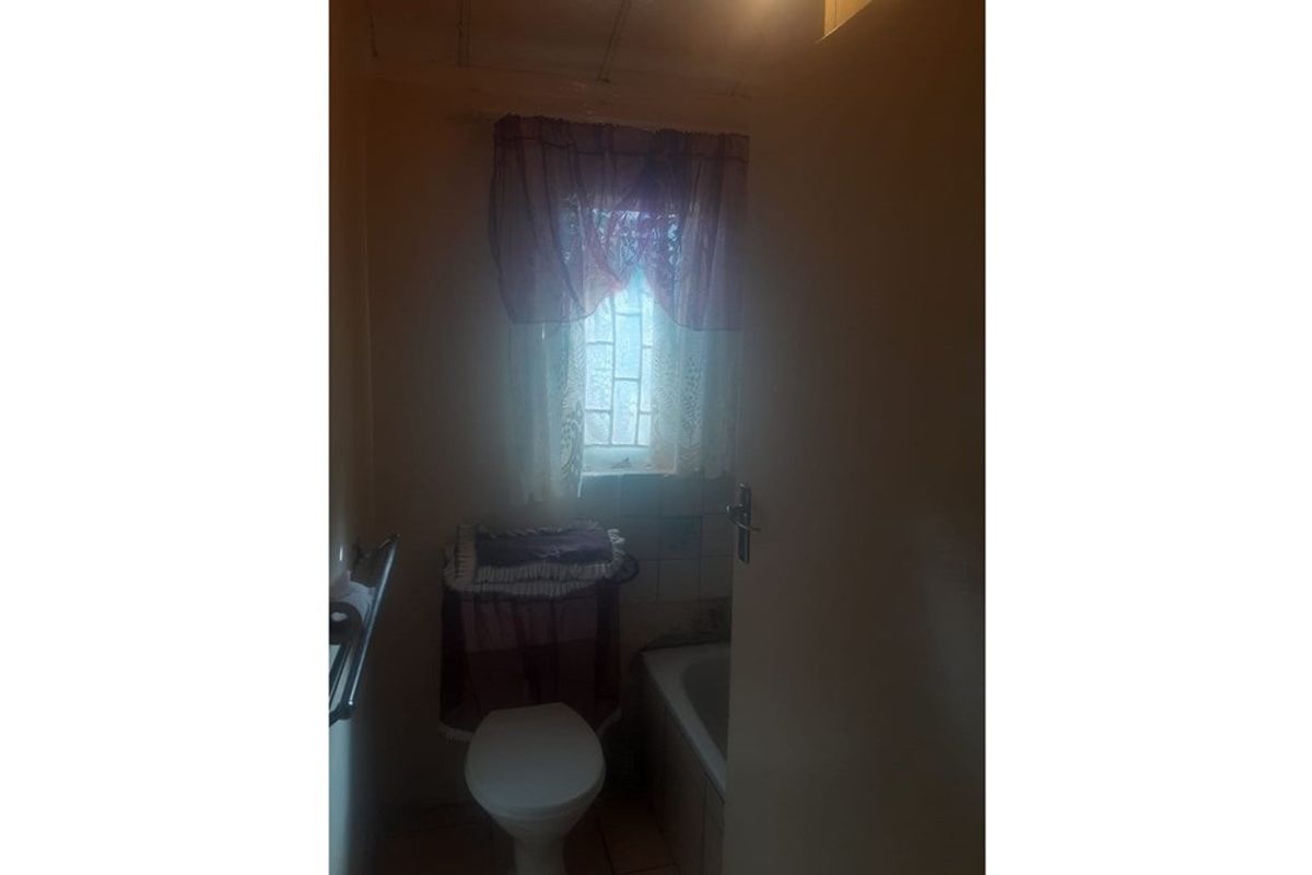 A compact bathroom featuring a bathtub and toilet, requiring updated lighting and finishes to improve the overall aesthetic and functionality.