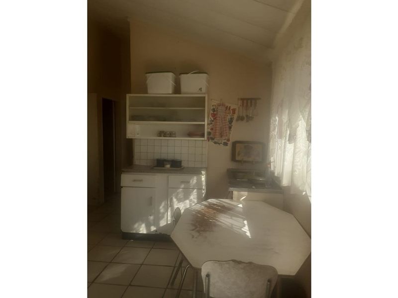 A dated kitchen area featuring built-in cabinetry, tiled splashbacks, and tiled flooring, offering potential for modernization and renovation.