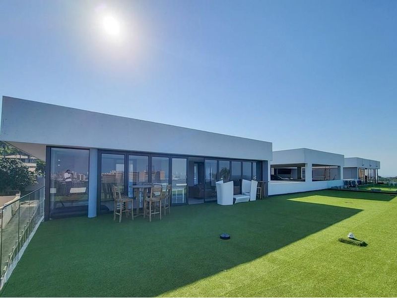 Spacious rooftop terrace featuring artificial turf, glass balustrades, and large sliding glass doors providing seamless indoor-outdoor flow.