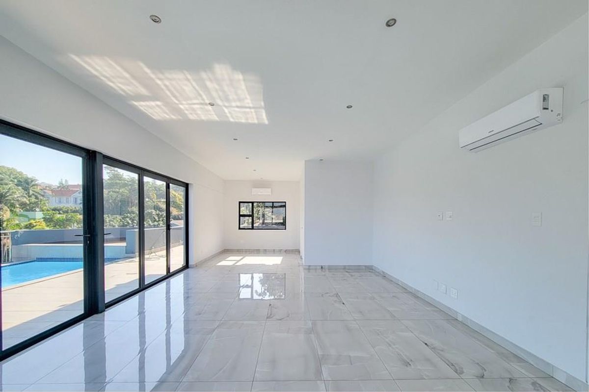 Spacious, bright open-plan living area featuring large format polished floor tiles, recessed lighting, split-system air conditioning, and expansive sliding doors leading to the pool area.