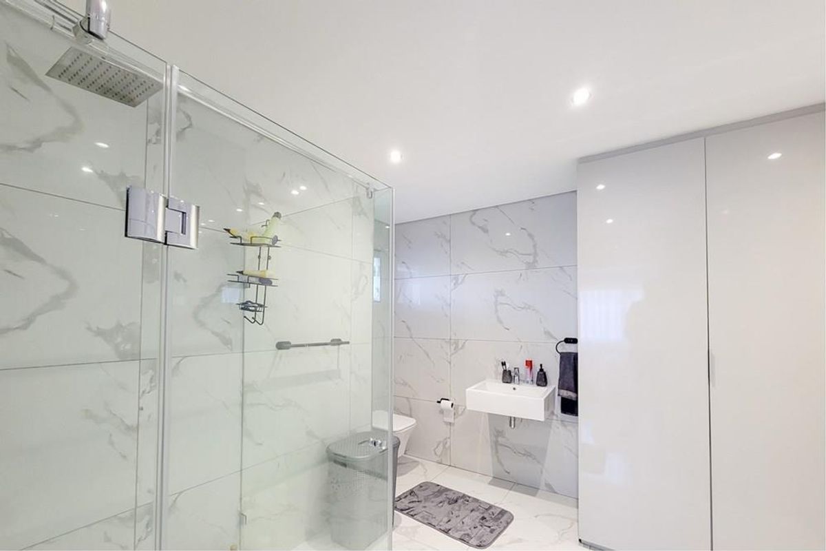 Modern penthouse bathroom featuring a glass-enclosed rain shower, wall-mounted basin, and sleek marble-look tiling with integrated storage cabinetry.