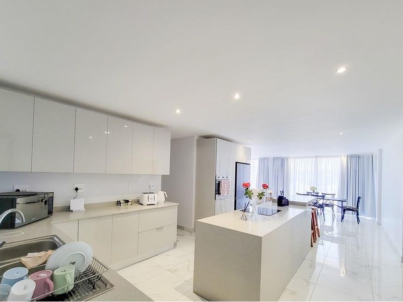 Modern open-plan kitchen featuring sleek cabinetry, a central island, stone countertops, and high-quality porcelain flooring, seamlessly flowing into the living and dining area.