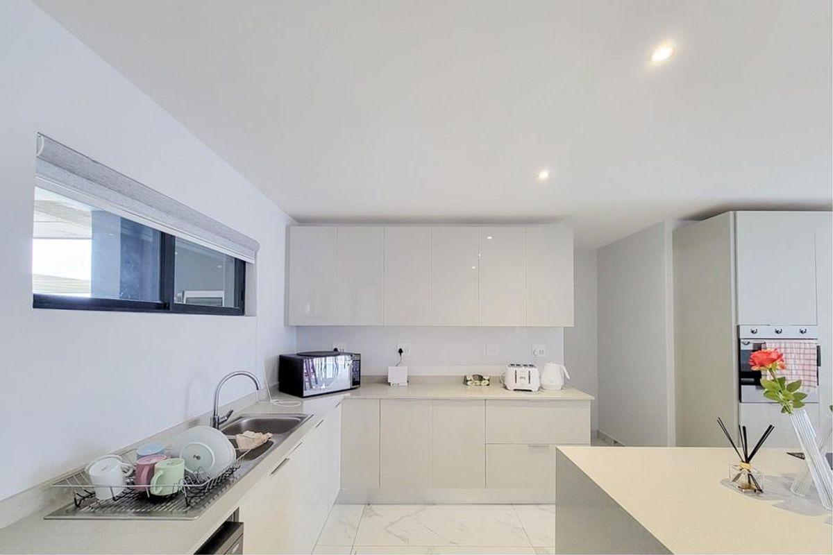 Modern kitchen featuring sleek high-gloss cabinetry, stone countertops, integrated oven, and polished marble-look tiled flooring with recessed lighting.