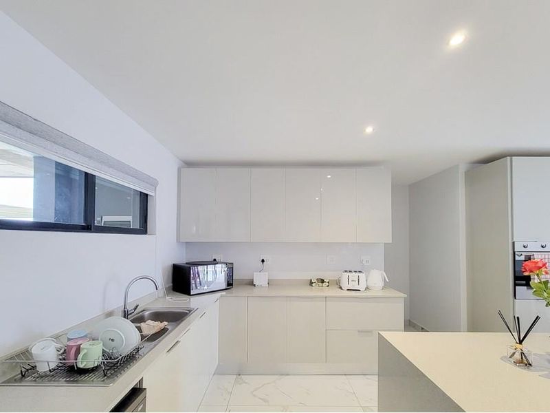 Modern kitchen featuring sleek high-gloss cabinetry, stone countertops, integrated oven, and polished marble-look tiled flooring with recessed lighting.
