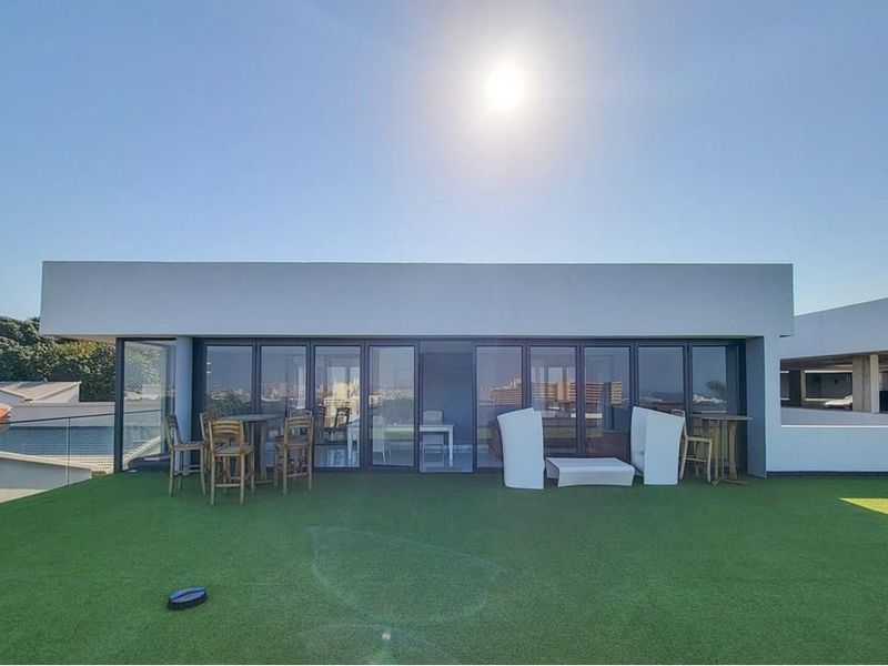 Spacious penthouse balcony featuring artificial turf, a modern glass balustrade, and large folding glass doors providing seamless indoor-outdoor flow.