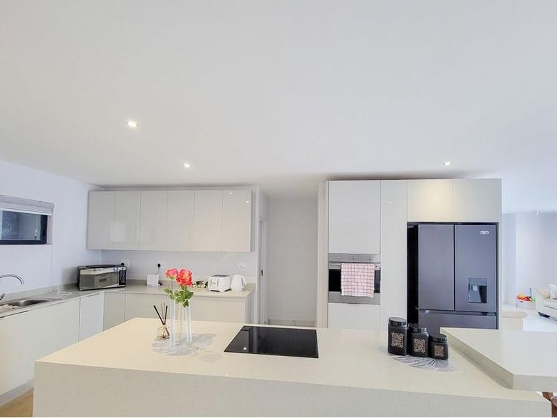 Modern open-plan kitchen featuring sleek gloss cabinetry, a central island with an induction hob, and high-quality quartz countertops in a bright, contemporary space.