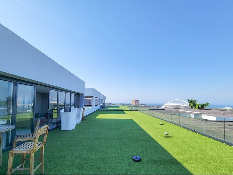 Spacious penthouse balcony featuring artificial turf, a modern glass balustrade, and expansive views of the surrounding area.