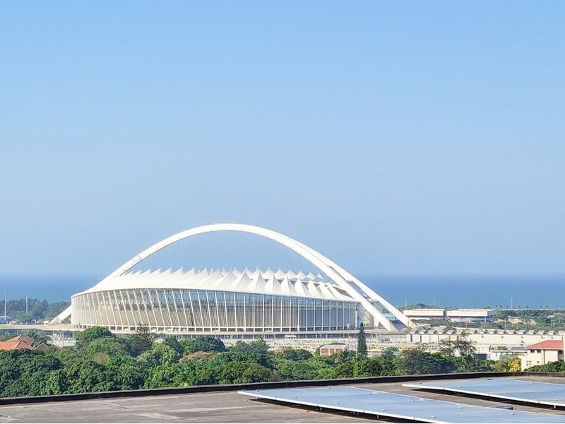 Elevated view overlooking the Moses Mabhida Stadium and the coastline, featuring solar panels installed on the foreground rooftop.