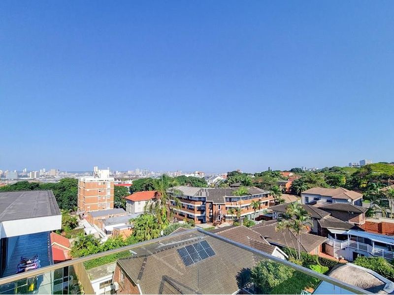 Elevated panoramic urban and suburban view captured from a penthouse balcony with a modern glass balustrade.