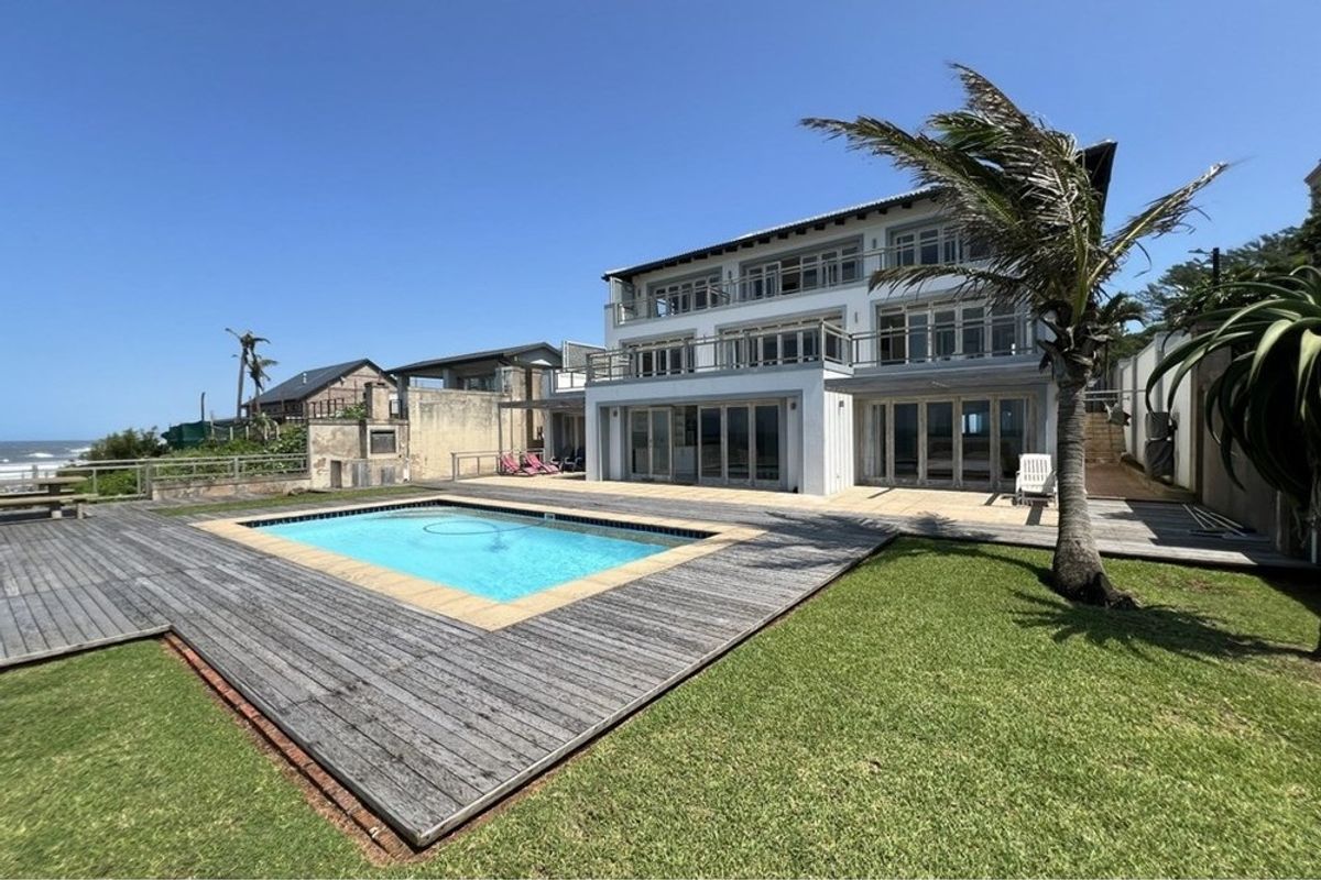 A multi-story coastal residence featuring a swimming pool, expansive timber decking, and tiered balconies overlooking the ocean.