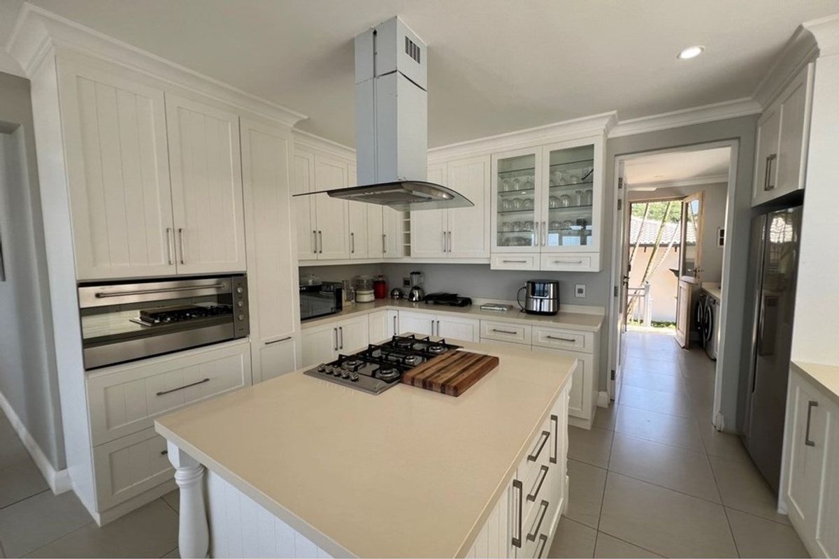 A well-appointed kitchen featuring white cabinetry, a central island with a built-in gas hob, and a stainless steel extractor fan.