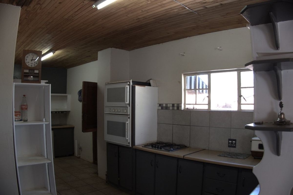 A dated kitchen featuring dark cabinetry, built-in double ovens, a gas hob, and a timber-clad ceiling, offering a functional layout with potential for modernization.