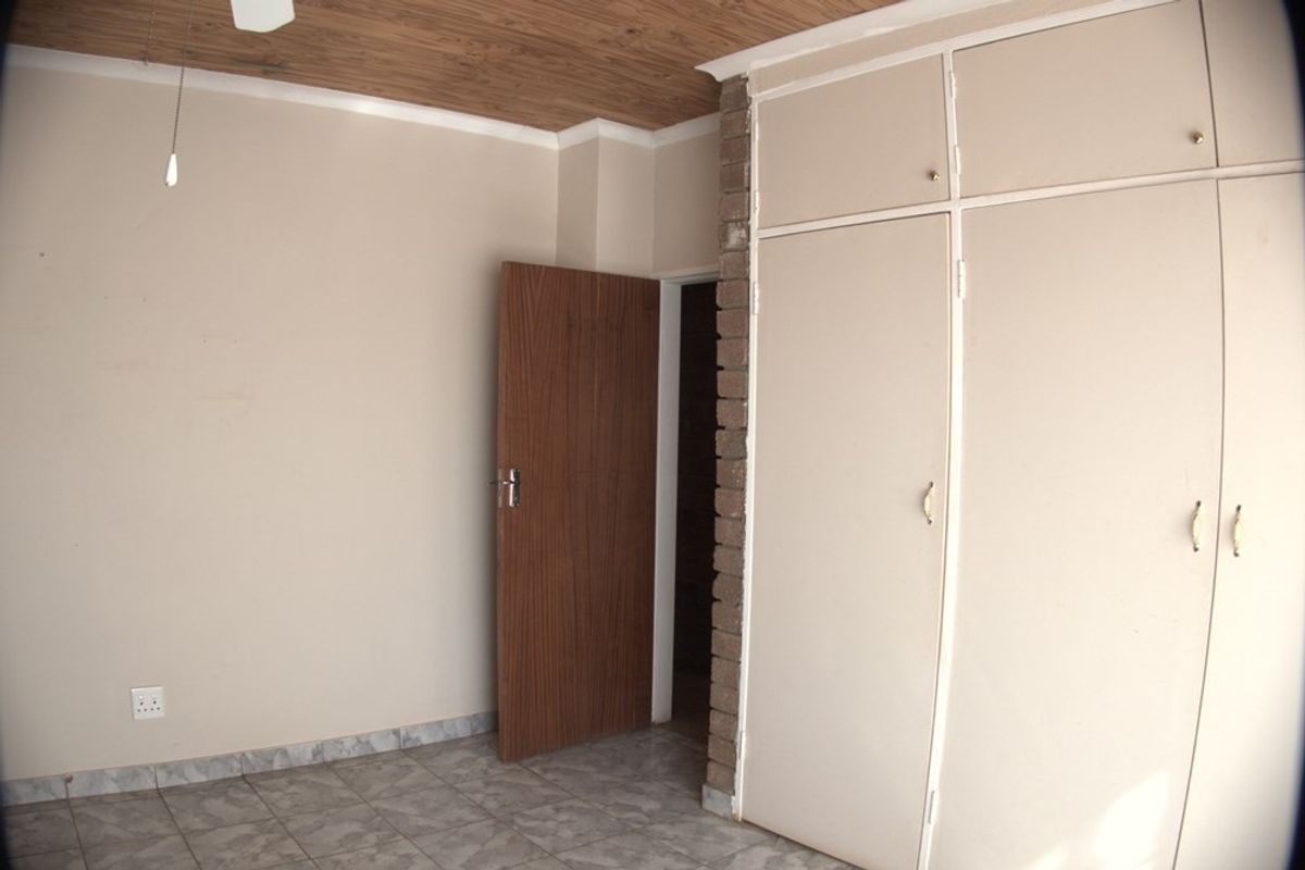 A bedroom featuring built-in cupboards, tiled flooring, and a wood-paneled ceiling.
