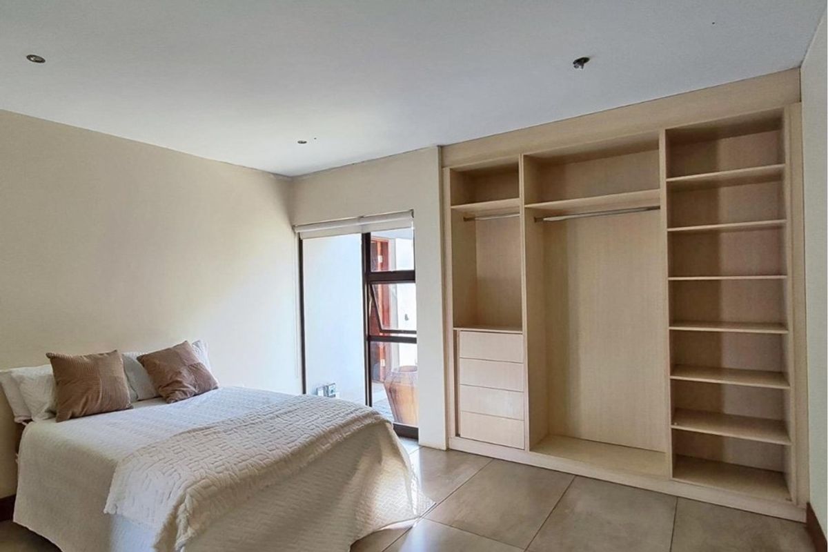 A bright bedroom featuring neutral tiled flooring, built-in light wood cabinetry with shelving and hanging space, and direct access to an outdoor area.