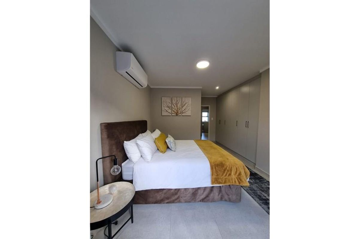A well-maintained bedroom featuring neutral tones, built-in cupboards, tiled flooring, and a wall-mounted air conditioning unit.