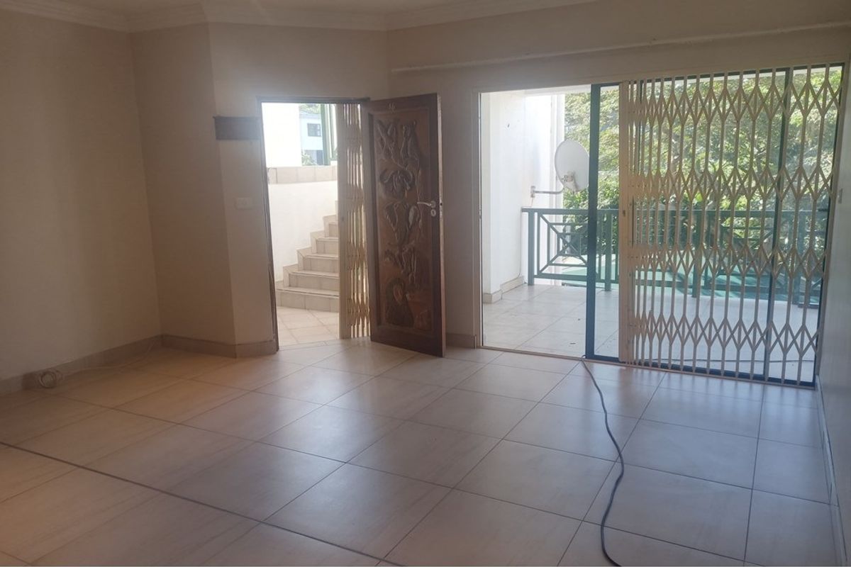 An empty living room featuring tiled flooring, a sliding glass door with a security gate, and direct access to an outdoor patio area.
