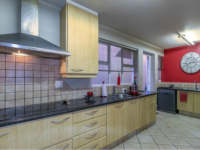 A functional kitchen featuring light wood cabinetry, granite countertops, a stainless steel extractor fan, and tiled flooring with a dedicated prep area.