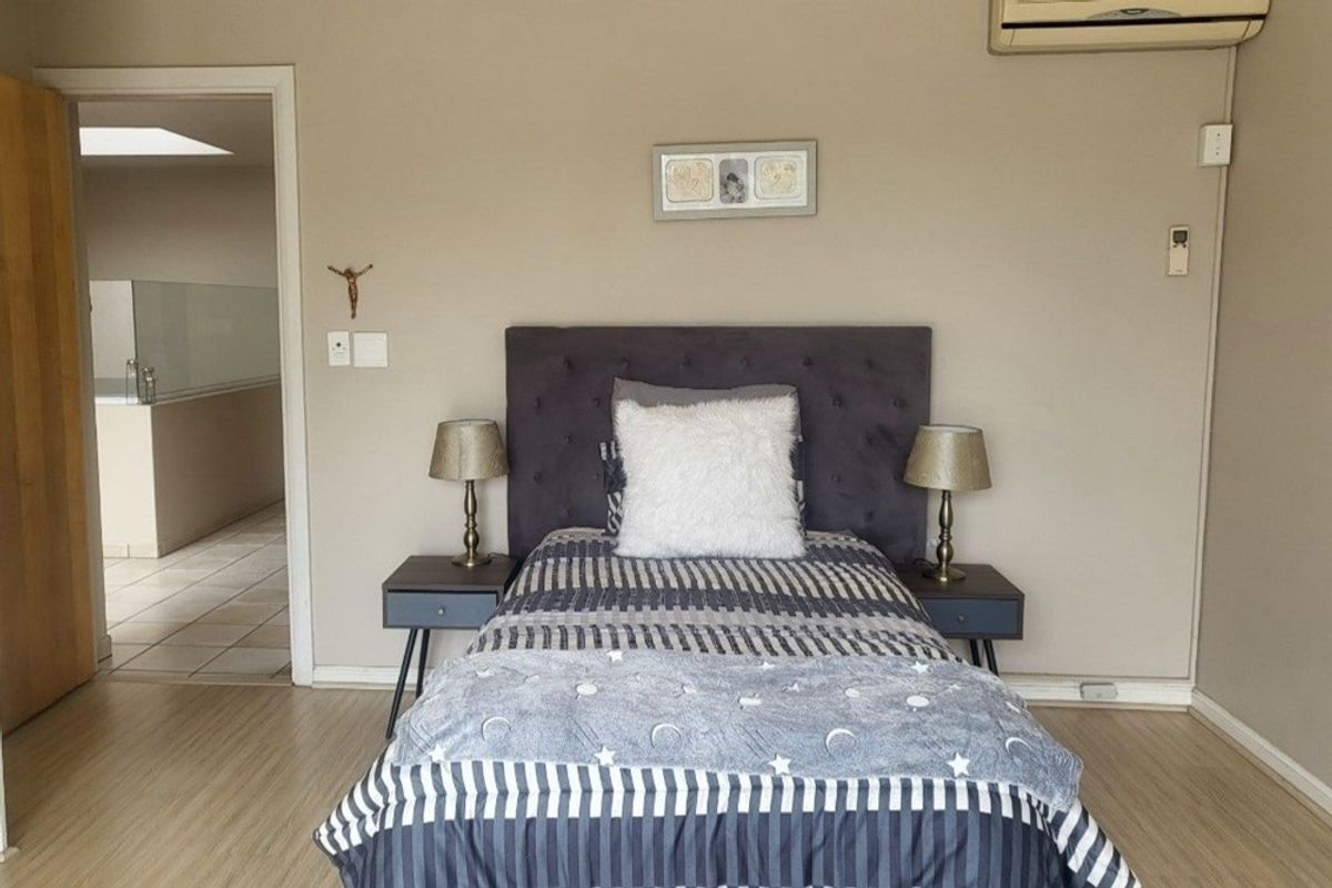 A bedroom featuring laminate flooring, neutral wall tones, and a wall-mounted air conditioning unit, with an adjacent view into a tiled bathroom area.