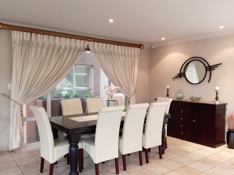 A well-maintained dining room featuring neutral wall tones, ceramic tiled flooring, and a large sliding glass door providing natural light.