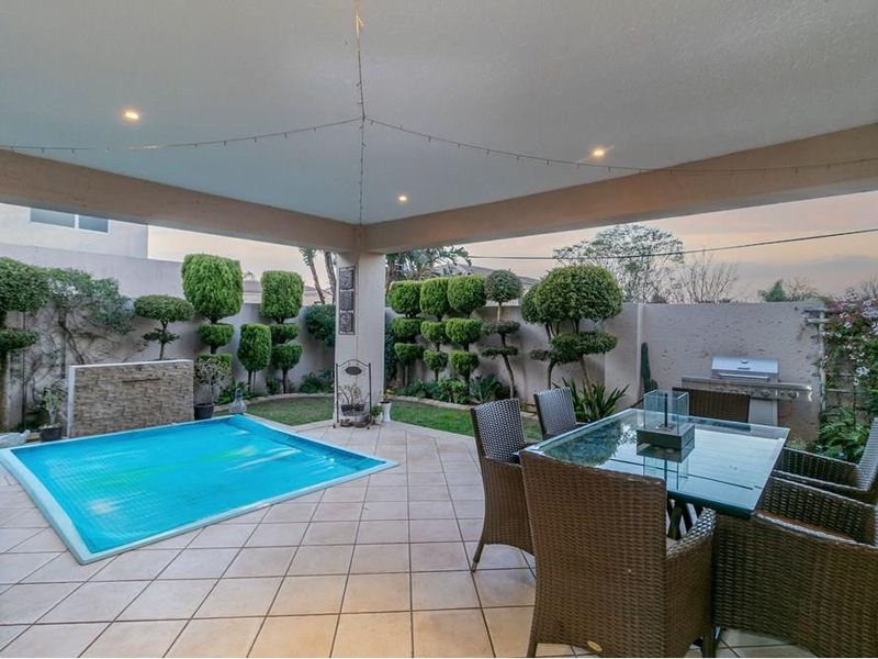 Covered patio area featuring tiled flooring, recessed lighting, a built-in barbecue, and a swimming pool set within a landscaped garden.