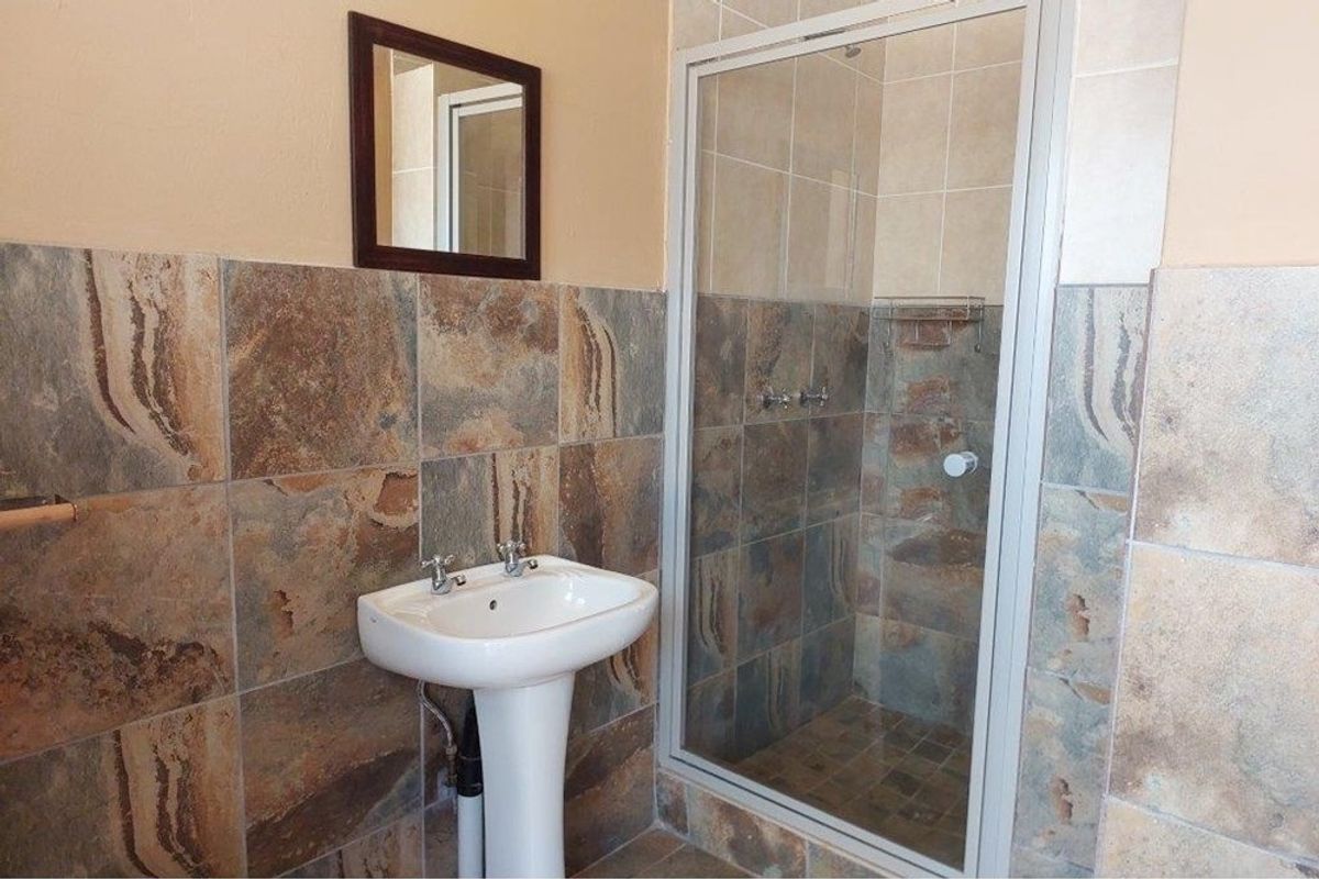 A functional bathroom featuring a pedestal basin, a glass-enclosed shower, and natural stone-style wall tiling.