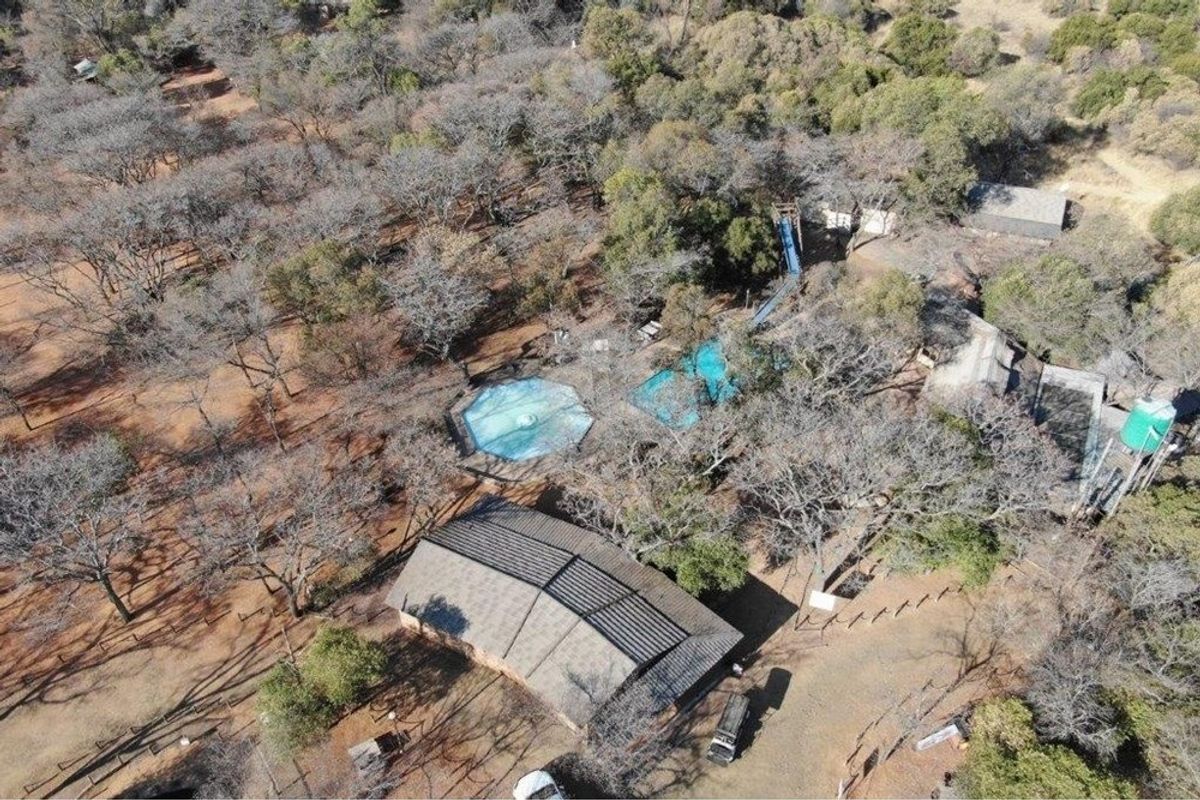 Aerial view of a farm property featuring a swimming pool, water slide, and multiple outbuildings set within a wooded landscape.