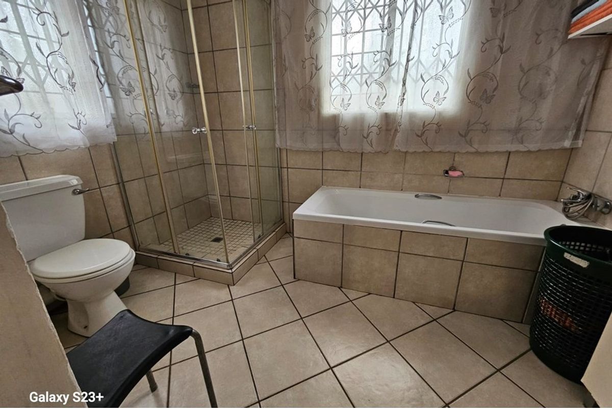 A functional bathroom featuring a tiled shower enclosure, a built-in bathtub, and a standard toilet with neutral wall and floor tiling.