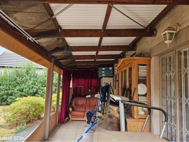 A covered patio area featuring timber beam ceilings, tiled flooring, and roll-down canvas blinds, providing a sheltered outdoor space overlooking the garden.