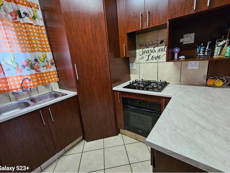 Compact kitchen featuring dark wood cabinetry, laminate countertops, a gas hob, built-in oven, and a double bowl sink with tiled flooring.