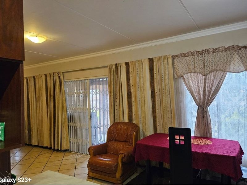 A living area featuring tiled flooring, ceiling cornicing, and a sliding glass door with an integrated security gate leading to the exterior.