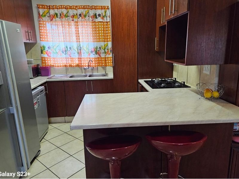 A functional kitchen featuring dark wood-look cabinetry, light laminate countertops, a gas hob, and tiled flooring with a breakfast nook area.