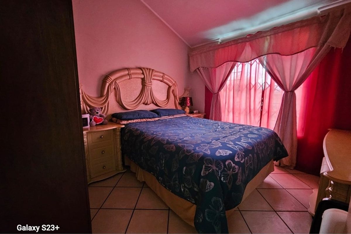 A bedroom featuring tiled flooring and a security gate over the window, providing a functional space with potential for modern updates.