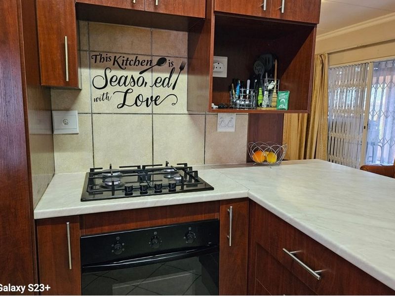 A functional kitchen area featuring dark wood cabinetry, a gas hob, a built-in oven, and a light-toned laminate countertop with a tiled backsplash.