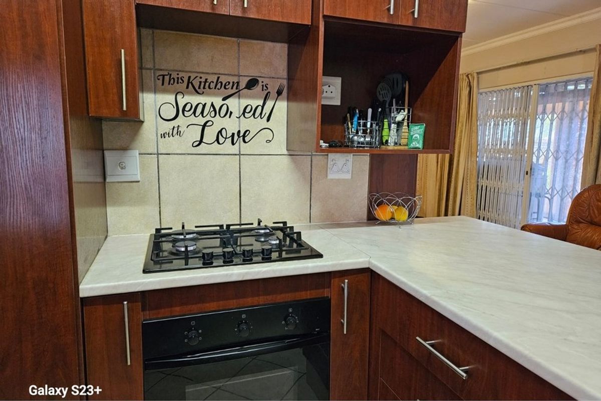 A functional kitchen area featuring dark wood cabinetry, a gas hob, a built-in oven, and a light-toned laminate countertop with a tiled backsplash.