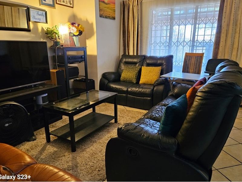 A comfortable living room featuring tiled flooring and a large sliding door with a security gate, providing access to the exterior.