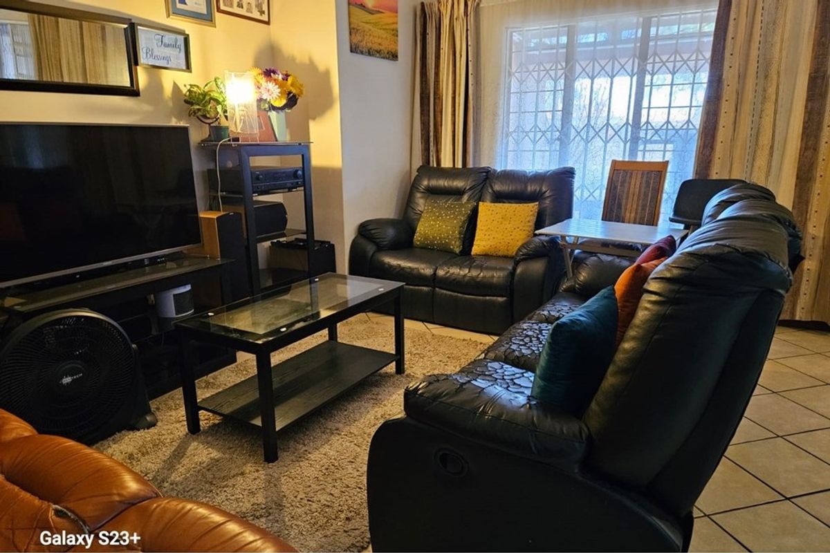 A comfortable living room featuring tiled flooring and a large sliding door with a security gate, providing access to the exterior.