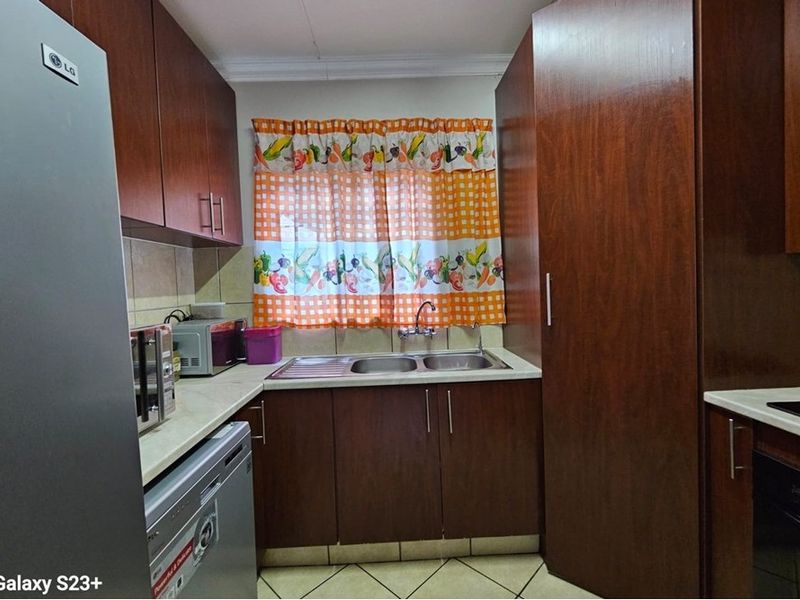 A functional kitchen featuring dark wood cabinetry, laminate countertops, a double basin sink, and tiled flooring with a tiled backsplash.