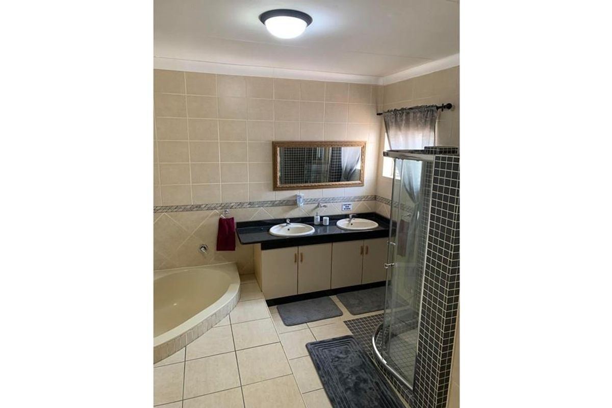 A functional bathroom featuring a double vanity with integrated sinks, a corner bathtub, and a separate glass-enclosed shower with tiled finishes.