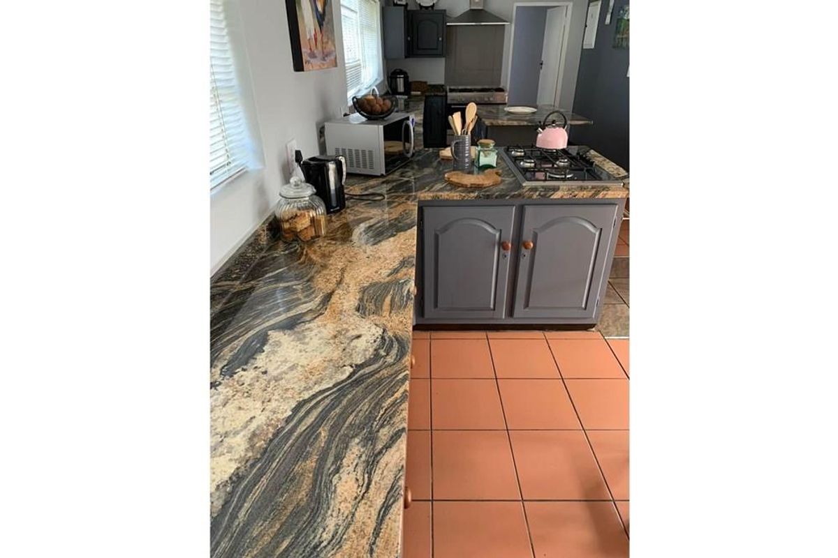 A functional kitchen featuring granite countertops, built-in gas hob, and grey cabinetry with terracotta floor tiles.